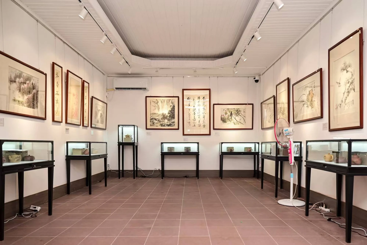 白墙展厅中的装裱书画与黑框玻璃陈列柜